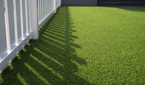 Sunlight and shadow of white wooden fence on green artificial turf surface in front yard of home, selective focus with copy space